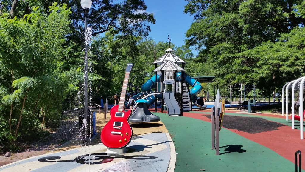 A playground on a sunny day. there is a giant guitar in front and the slides structure behind has keyboard printed roof. There is a water splash park. 