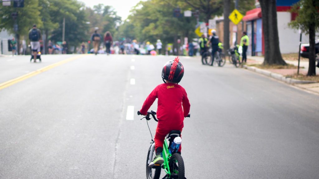A young person in a superhero costume rides a bicycle down a car-free georgia ave NW during DC's first Open Streets event