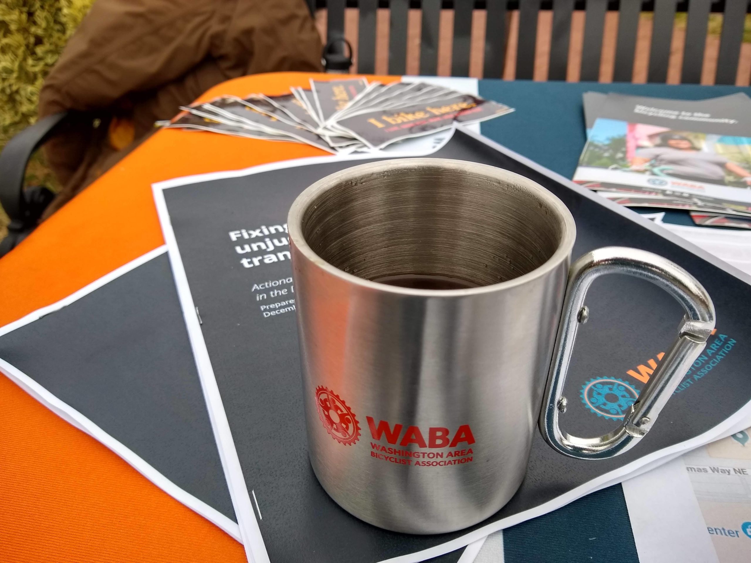 A new metal WABA mug sits on printed docuements that are branded WABA materials on a table outside