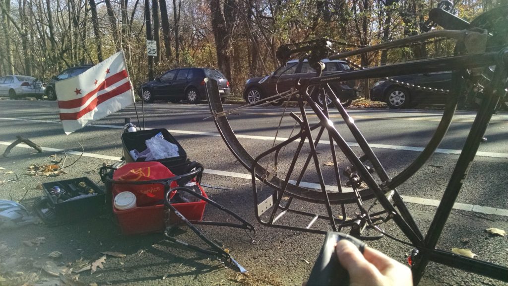 Kinda washed out photo of a back bike wheel missing the wheel, the person is sitting by the road fixing her flat